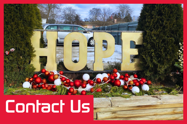 A festive outdoor display with the word "HOPE" in large gold letters. The background shows a residential setting with a car and fence. The text "Contact Us" is at the bottom of the image.