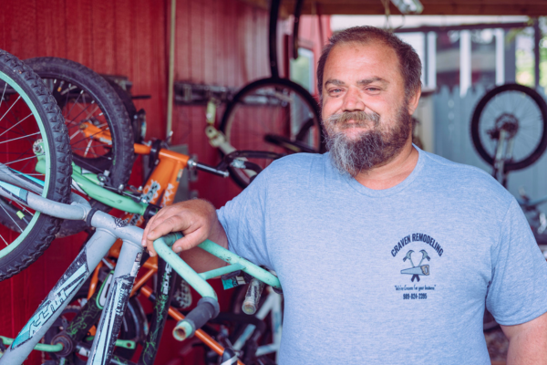Donate – Bikes A guest from the men's crisis shelter stands in front of the bike repair station at Midland's Open Door.