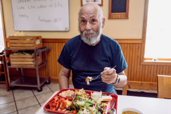 An older man eats a red tray filled with healthy food at the Open Door's community soup kitchen.
